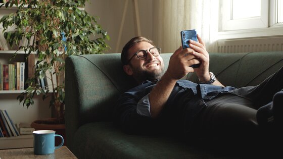 Mann ligger på sofaen med en mobil