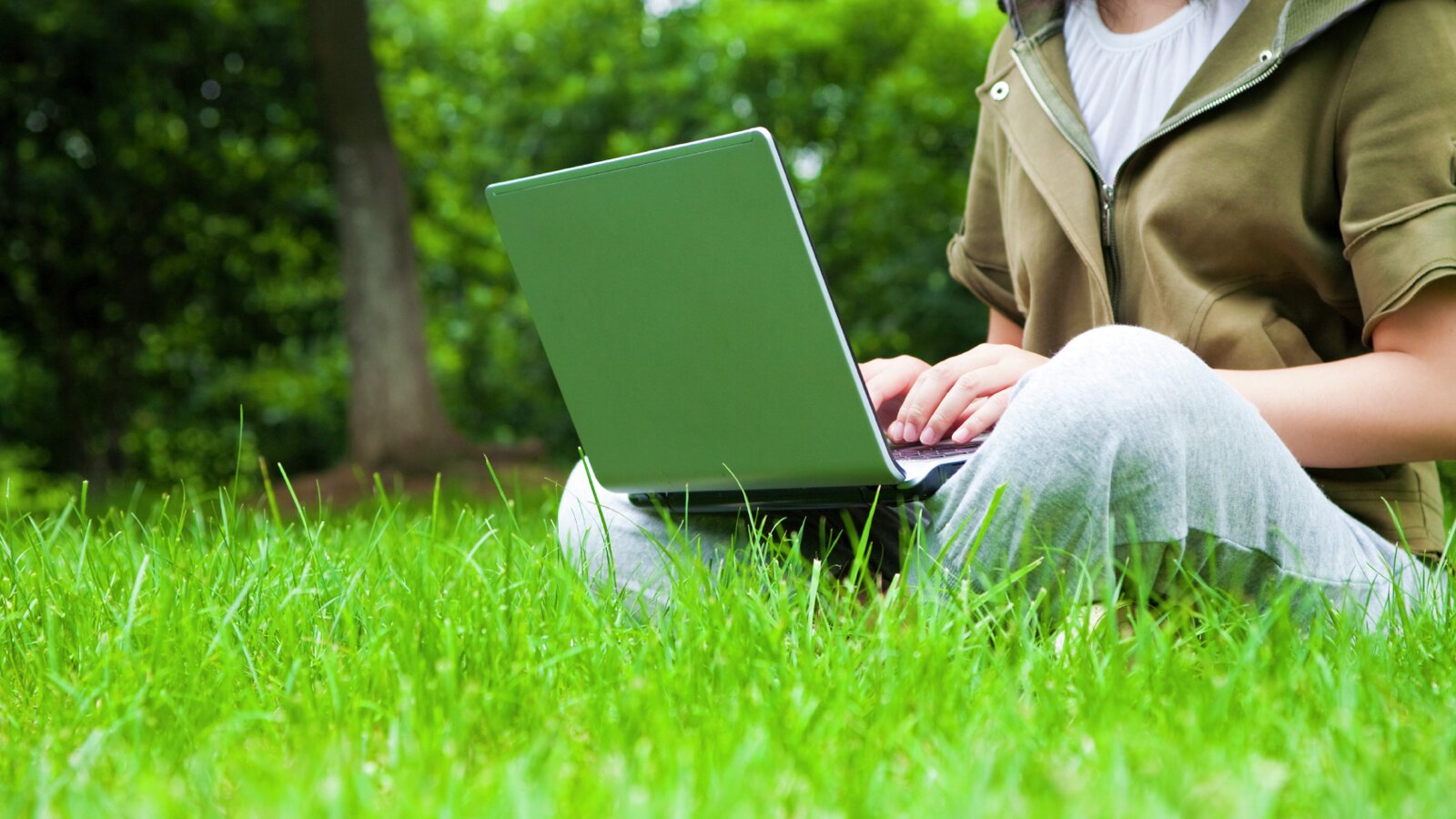 Person sitter i gresset med laptop i fanget