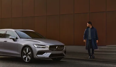 Man står på trottoar och tittar på en silvrig Volvo V60.