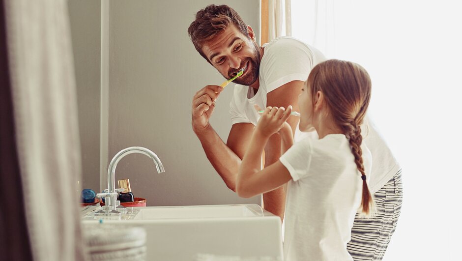Pappa och dotter borstar tänderna i badrummet