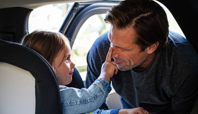 Flicka i bakåtvänd bilbarnstol petar sin pappa på näsan