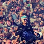 Helle-Viv crowd surfer på konsert. Publikum bærer henne på skuldrene sine i rullestolen. Hun smiler bredt.