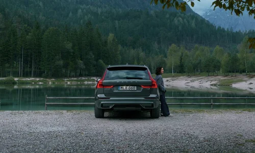 Kvinna lutar sig mot mörk Volvo parkerad i natur.