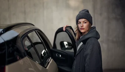 Kvinna med mörka ytterkläder vid bildörr till Volvo EX40.