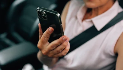 Kvinna sitter i bilen med säkerhetsbältet på sig och tittar i mobiltelefonen.
