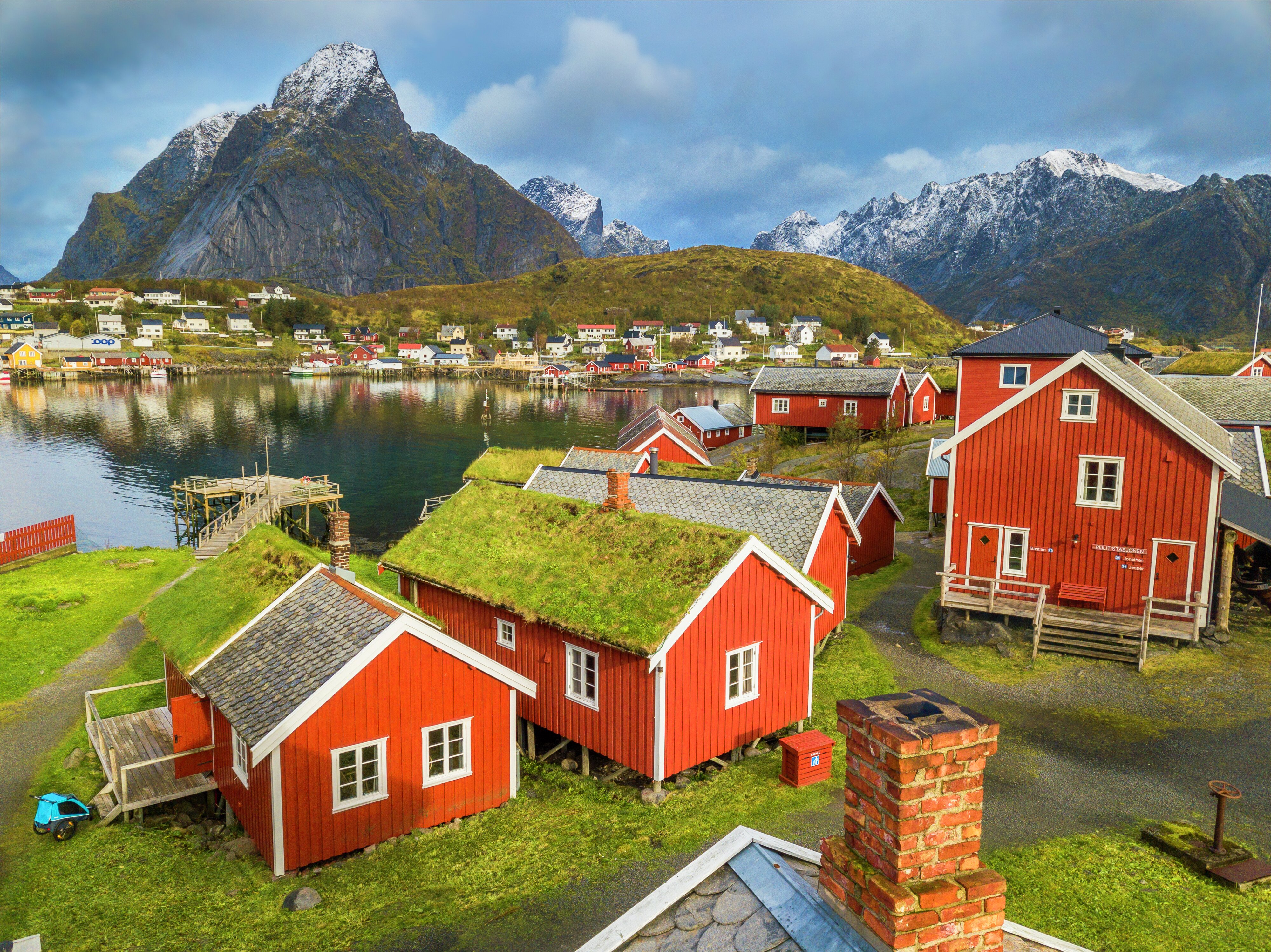 Reine Rorbuer: several small red houses by the sea, with mountains and village in the background.