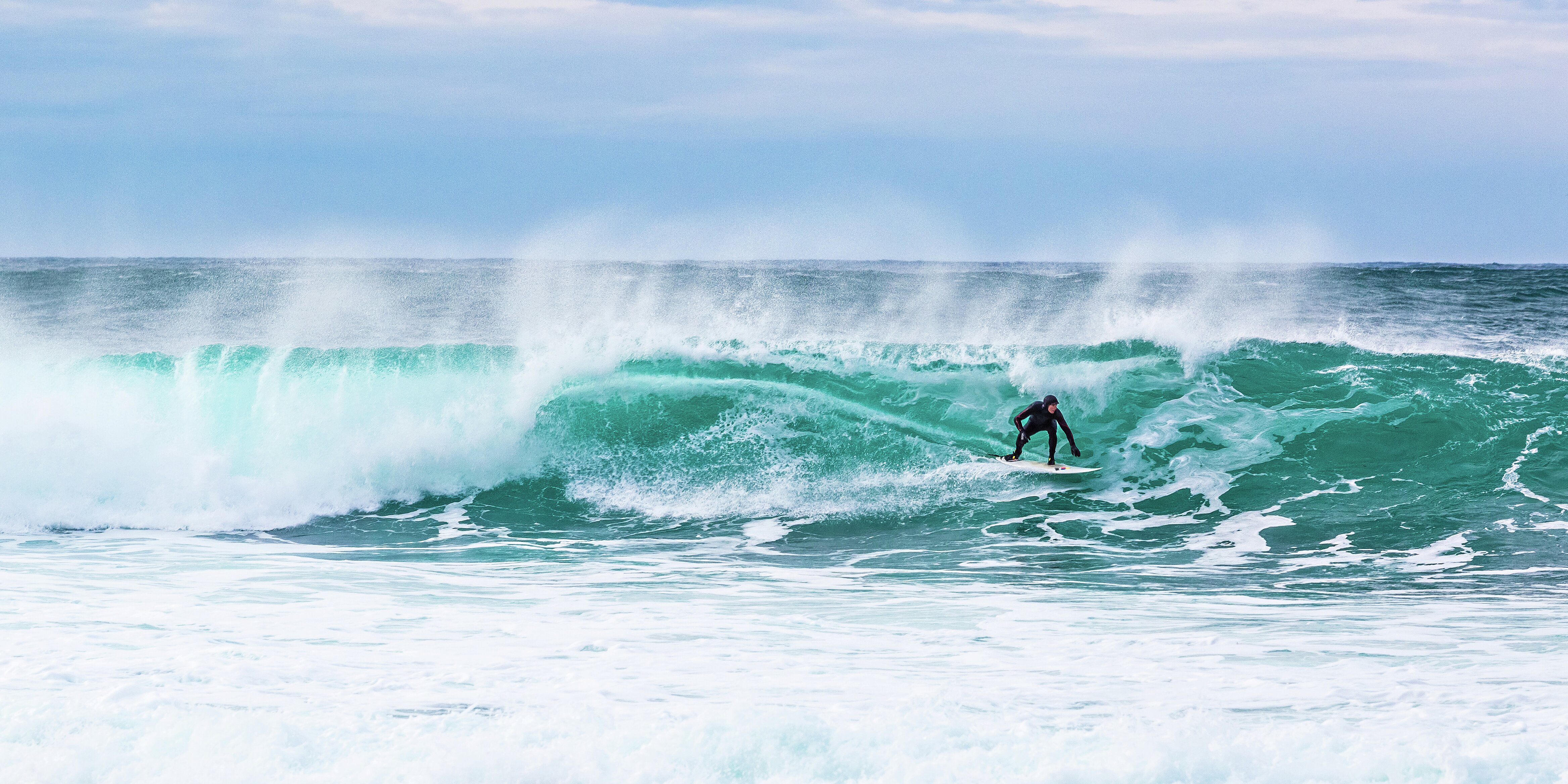 Surfing i det kalde nord: en surfer på en stor bølge, blå himmel bak. 