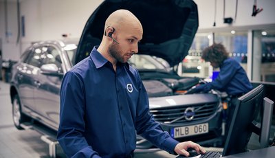 Servicetekniker står vid dator, en annan tekniker inspekterar motorn på en Volvo i bakgrunden