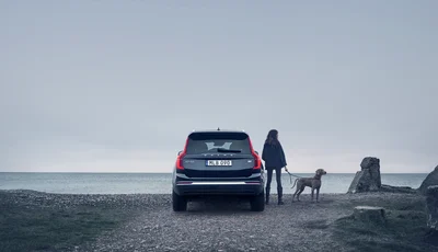Kvinna med hund i koppel står bredvid Volvo XC90 vid havet.