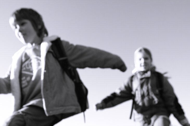 Barn med skolesekker som løper, sort/hvitt