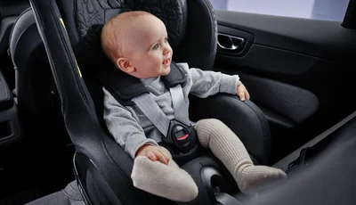 Leende bebis sitter i bakåtvänd bilbarnstol.