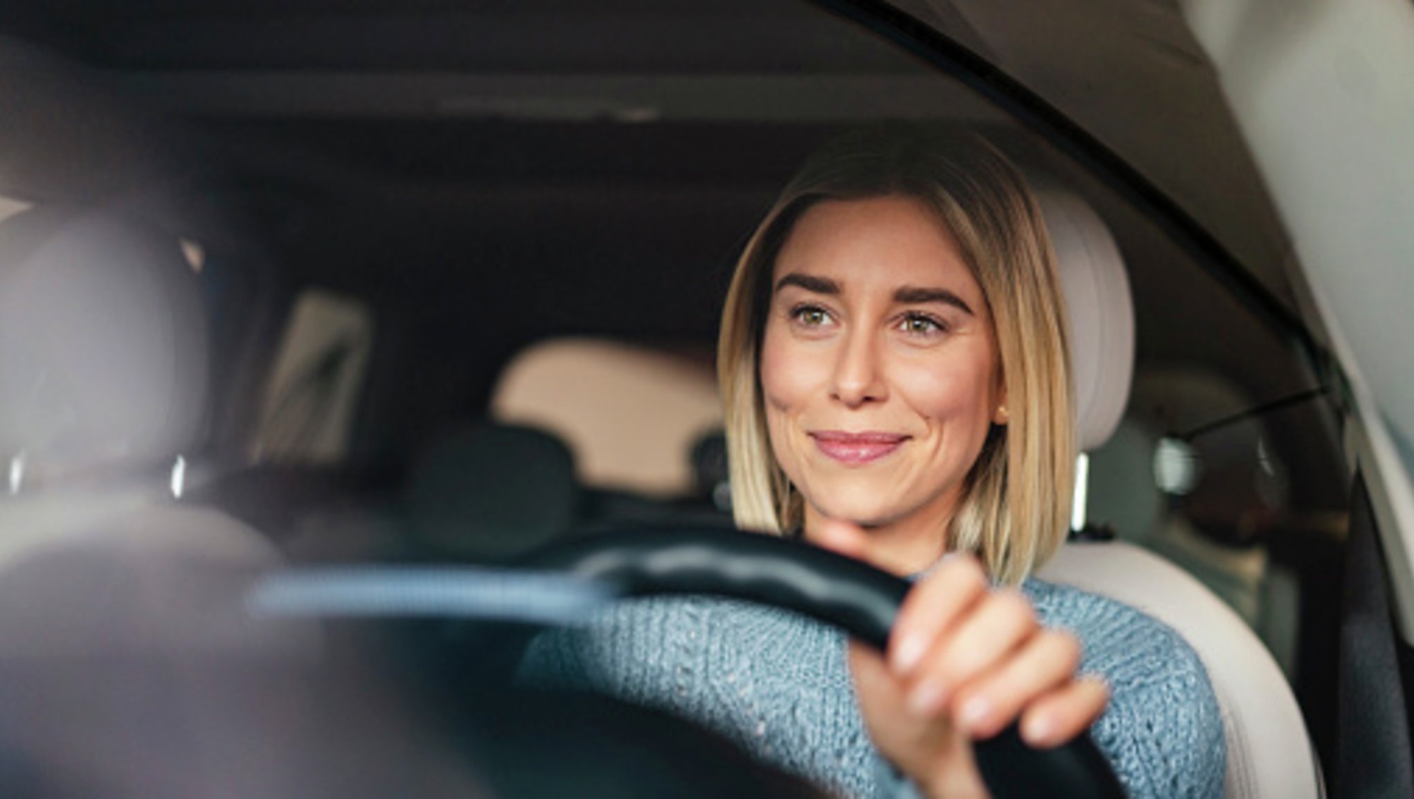 Moteris šypsosi vairuodama automobilį.