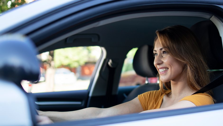 Kvinde sidder i en bil og smiler 