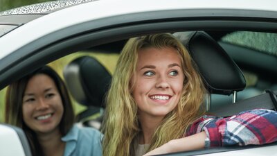 Kaksi hymyilevää naista katsovat ulos autosta.